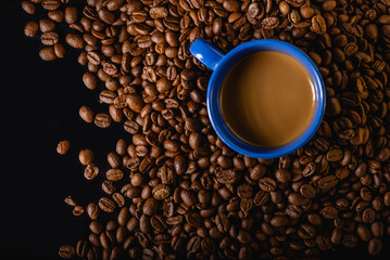 Top view above of Black hot coffee with milk foam for morning beverage menu in blue ceramic cup with coffee beans roasted in burlap sack bag on dark grunge table background. Flat lay with copy space.
