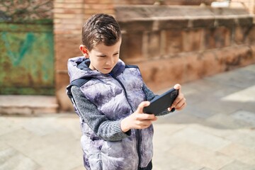 Blond child playing video game by the smartphone at street