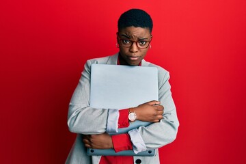 Young african american businesswoman holding laptop skeptic and nervous, frowning upset because of...