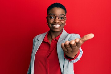 Young african american woman wearing business jacket and glasses smiling friendly offering...