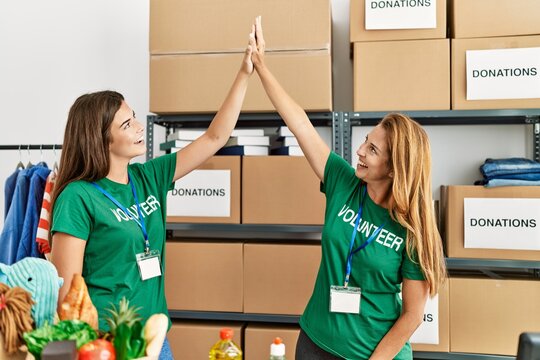 Mother and daughter wearing volunteer uniform high five raised up hands at charity center - Powered by Adobe