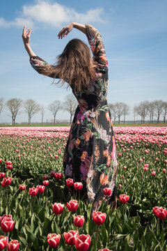 Portrait of woman dancing in floral dress standing in dutch field of tulips in spring