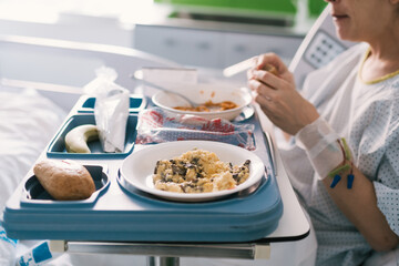 young woman who is hospitalized eating in the bed in the room the light meal that the nurses have...