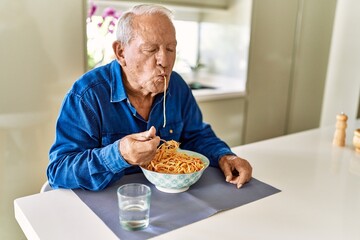 Senior man eating spaghetti at kitchen