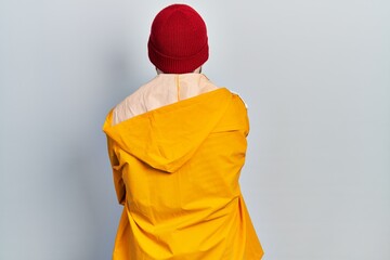Caucasian man with beard wearing yellow raincoat standing backwards looking away with crossed arms