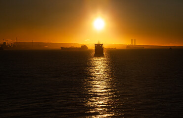 Obraz premium Ships at sea near the coast on the horizon in the yellow light of the setting sun.