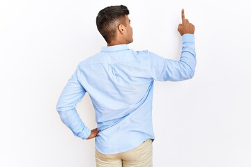 Young hispanic man wearing business shirt standing over isolated background posing backwards...