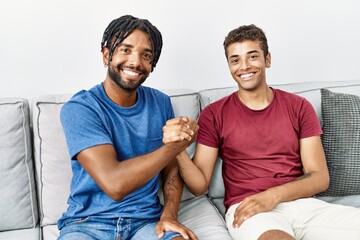 Two men friends smiling confident shake hands sitting on sofa at home