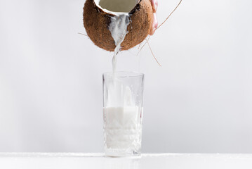 Coco abierto lleno de leche que se derrama sobre un vaso 