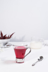 Una taza transparente de té de bayas y leche sobre una mesa blanca.
