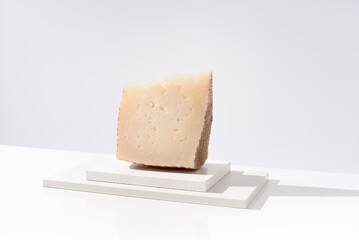 Trozo de queso manchego de oveja curado sobre una mesa blanca. Aperitivo español	