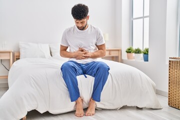 Young arab man suffering for stomachache sitting on bed at bedroom