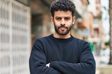 Young arab man with relaxed expression standing with arms crossed gesture at street