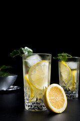Dos vasos de refrescante zumo de limón, cóctel de frutas con rodajas de limón y hielo sobre fondo negro