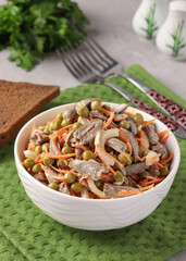 Salad with chicken hearts, canned peas, onions and carrots in a white bowl