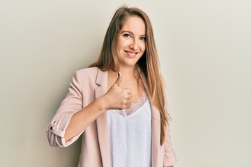 Fototapeta premium Young blonde woman wearing business jacket and glasses doing happy thumbs up gesture with hand. approving expression looking at the camera showing success.