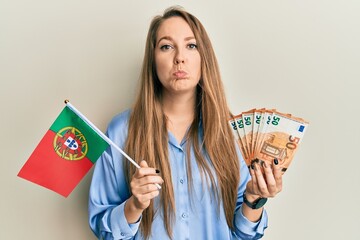 Young blonde woman holding portugal flag and euros banknotes depressed and worry for distress,...