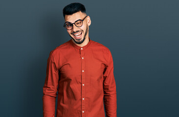 Obraz premium Young hispanic man with beard wearing business shirt and glasses winking looking at the camera with sexy expression, cheerful and happy face.