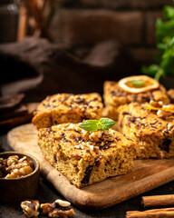 Pumpkin blondie bars with chocolate and walnuts close-up. Brownie pie slices on a serving wooden board on the dark culinary background. Baking for Thanksgiving	