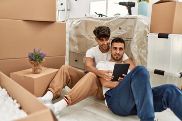 Two hispanic men couple smiling confident using touchpad at new home