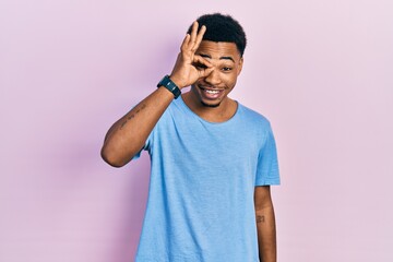 Fototapeta premium Young african american man wearing casual blue t shirt doing ok gesture with hand smiling, eye looking through fingers with happy face.