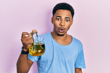 Young african american man holding olive oil can scared and amazed with open mouth for surprise,...