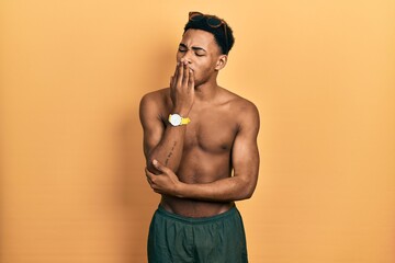 Young african american man wearing swimwear and swimmer glasses bored yawning tired covering mouth...