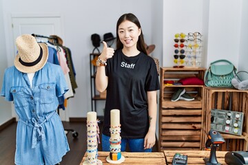 Young asian woman working as manager at retail boutique doing happy thumbs up gesture with hand. approving expression looking at the camera showing success.