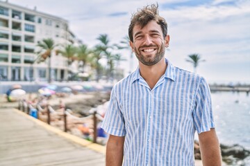 Fototapeta premium Young hispanic man smiling happy standing at the beach.
