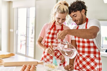 Young couple smiling happy pouring water to make dough for homemade bread at kitchen.