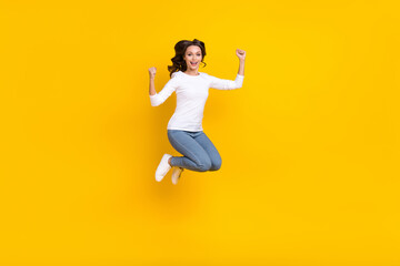 Fototapeta na wymiar Photo of sweet lucky woman wear white shirt rising fists jumping high isolated yellow color background