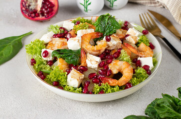 Salad with shrimps, pineapple, feta and pomegranate seeds in a plate on green lettuce leaves, on a gray background