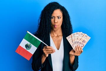 Middle age african american woman holding mexico flag and mexican pesos banknotes making fish face...