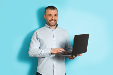 Middle Aged Man Using Laptop Computer Standing Over Blue Background