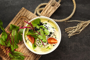 Mashed potatoes with fish in cream sauce, tomatoes and beetroot leaves in paper container on wood board isolated on dark background. Healthy food delivery service and daily ration concept.