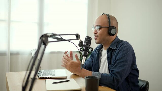Content creator asia man host streaming his a podcast on laptop with headphones and condenser microphone interview guest conversation at home broadcast studio. Male blogger recording voice over radio