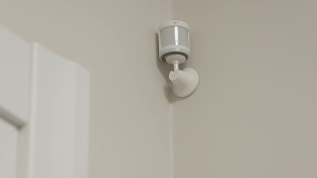 Smart home wireless motion sensor for alarm system and smart home automation, small plastic white motion detector installed in the living room. High quality 4k footage