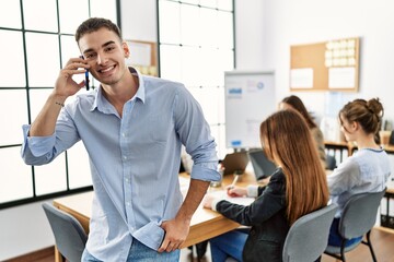Young businesman smiling happy talking on the smartphone while partners work at the office.