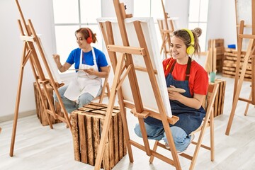 Two artist student women smiling happy and listening to music painting at art school.