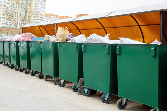 Green dumpsters full of rubbish under plastic roof in residential of russian city. Municipal waste bins.