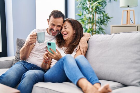 Middle age man and woman couple using smartphone and drinking coffee at home