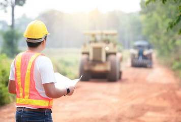 Civil engineers in reflective vests, wearing helmets, overseeing tractors, graders, and trucks for road clearing. Prepare the road construction site