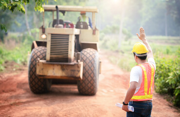 Civil engineers in reflective vests, wearing helmets, overseeing tractors, graders, and trucks for road clearing. Prepare the road construction site
