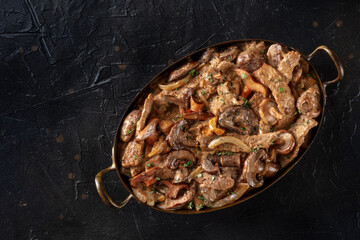 Mushroom beef stroganoff, a casserole of boletus, champignons, and meat, with cream sauce, shot from the top on a dark background with copy space