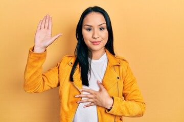 Beautiful hispanic woman with nose piercing wearing yellow leather jacket swearing with hand on...