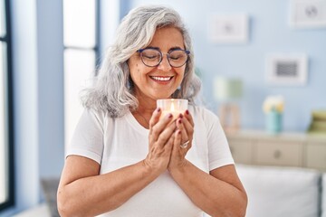 Middle age woman smelling aromatic candle at home