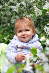 Happy smiling little baby girl in mother’s hands on background of blooming garden with apple trees.