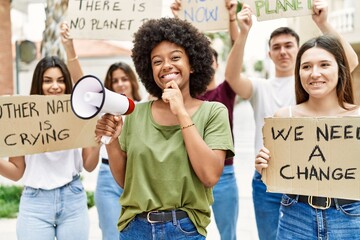 Group of young friends protesting and giving slogans at the street serious face thinking about question with hand on chin, thoughtful about confusing idea