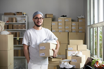 Confident young Asian man retail seller, entrepreneur, online store drop shipping small business owner looking at camera standing in delivery shipping warehouse with parcel boxes. - 499591721