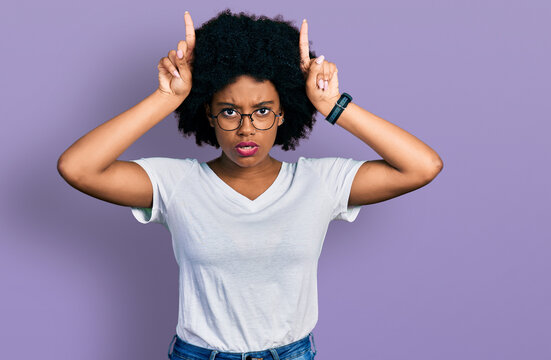 Young african american woman wearing casual white t shirt doing funny gesture with finger over head as bull horns